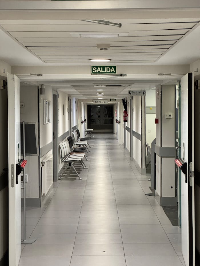 Long empty hospital corridor with exit sign, emphasizing cleanliness and sterility.