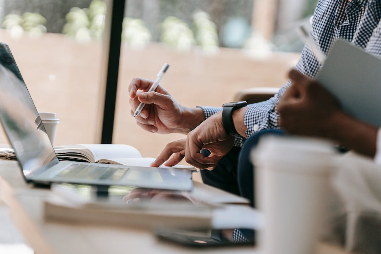 Close-up of colleagues discussing work using a laptop and notebook in an indoor office setting.